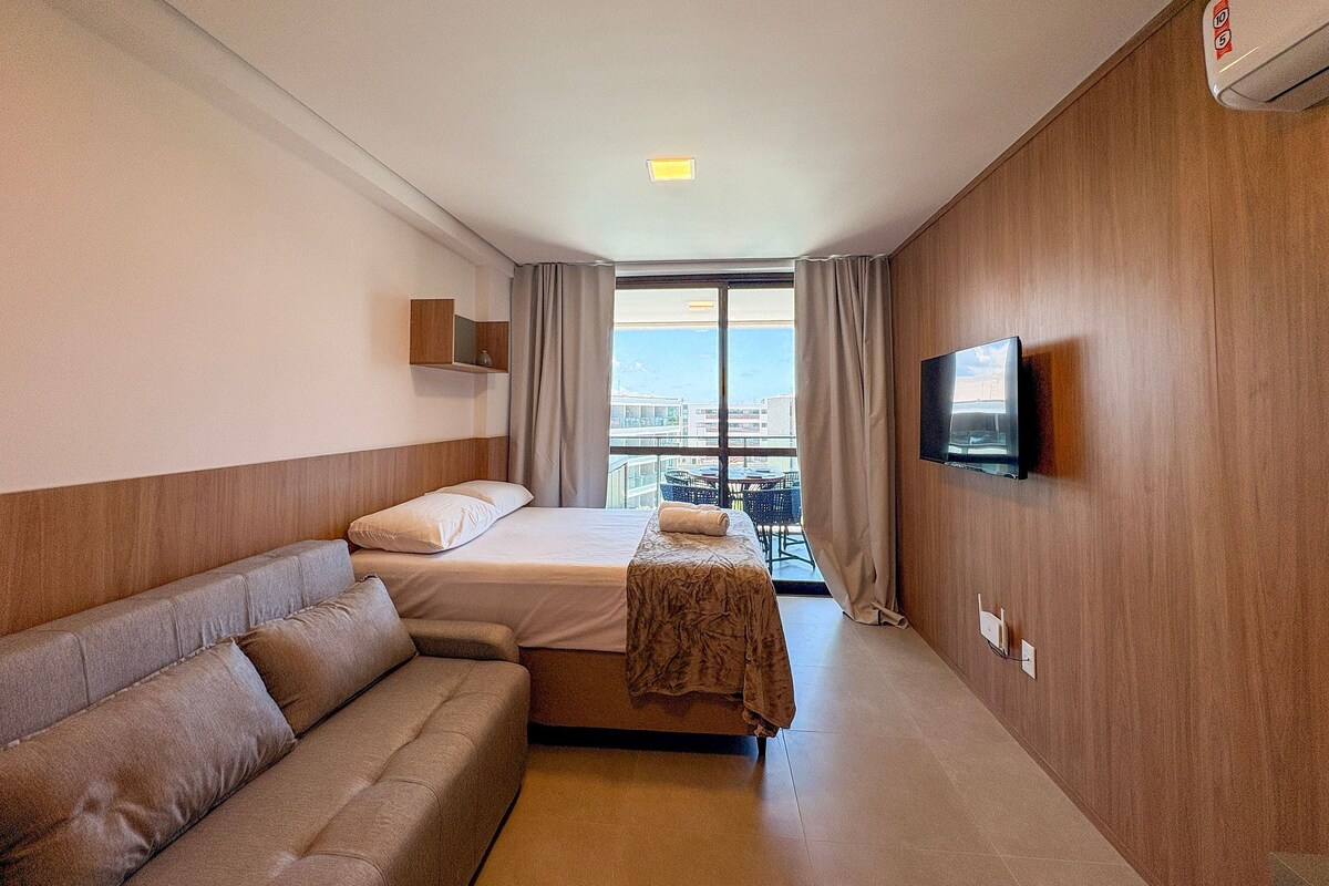 A hotel room with a bed, a sofa, a TV, and a balcony with a view.