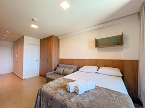 A hotel room with a bed, a seating area, a wardrobe, and a mirror on the wall. - Beach Class Solare Muro Alto (Ipojuca)