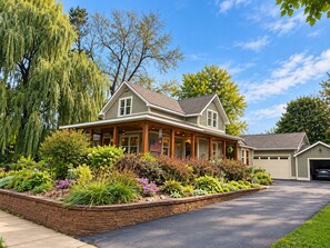 Ein zweistöckiges Haus mit überdachter Veranda, Garage und einem angelegten Vorgarten.