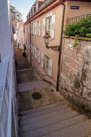 Une rue étroite, bordée de bâtiments des deux côtés, avec un regard d’égout et un lampadaire.