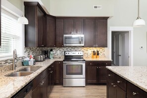A modern kitchen with dark wood cabinets, stainless steel appliances, and a granite countertop. - 4BR Corolla Light Retreat w/ Hot Tub & Game Room (Corolla)