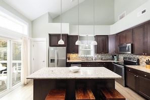 A modern kitchen with dark wood cabinets, a granite countertop, stainless steel appliances, and pendant lighting. - 4BR Corolla Light Retreat w/ Hot Tub & Game Room (Corolla)
