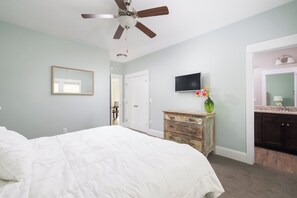 A bedroom with a bed, a ceiling fan, a dresser, a television, and a bathroom door. - 4BR Corolla Light Retreat w/ Hot Tub & Game Room (Corolla)