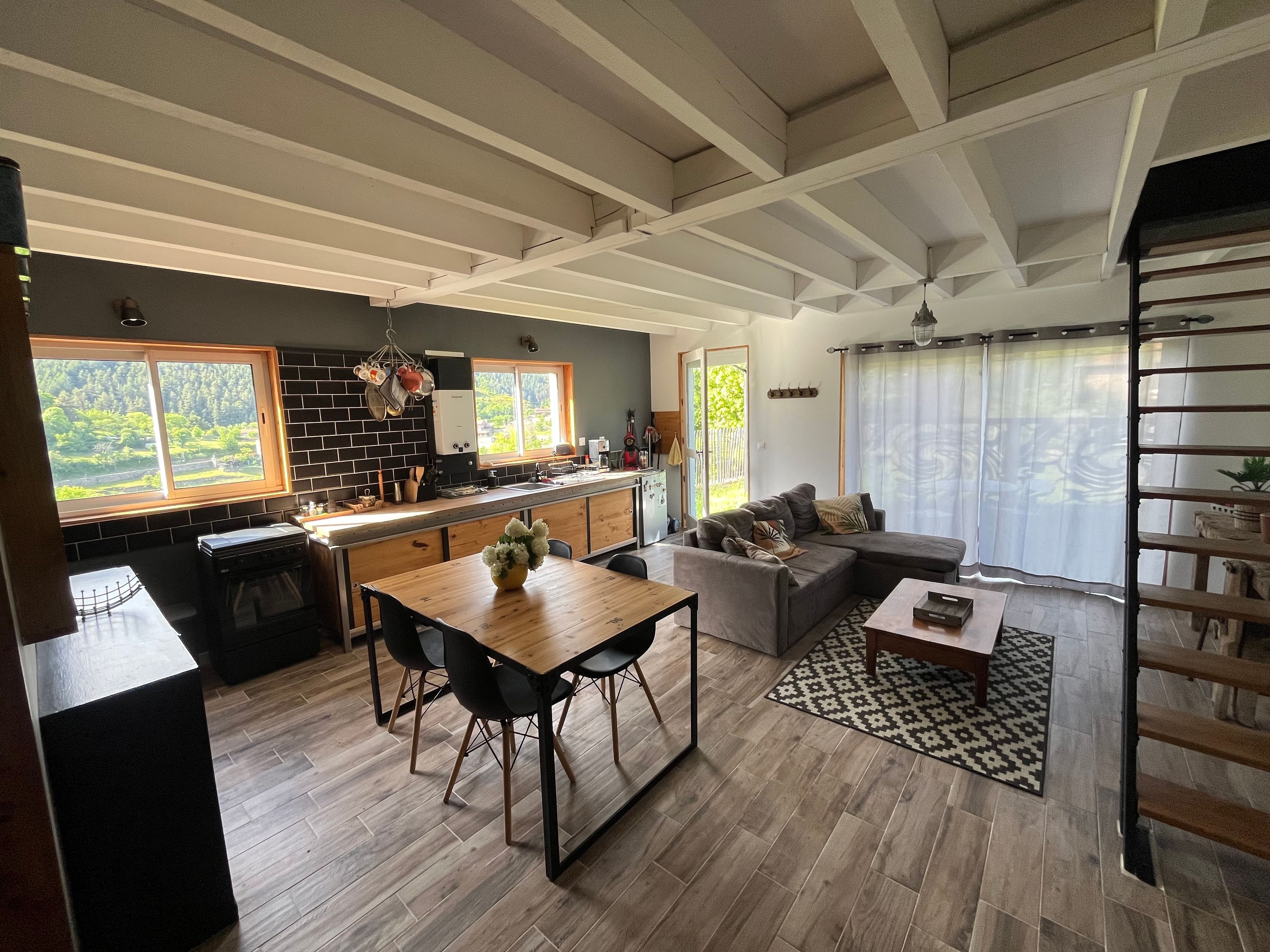 A modern kitchen with a dining area, a living room with a sofa, and a staircase.