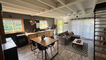 A modern kitchen with a dining area, a living room with a sofa, and a staircase.