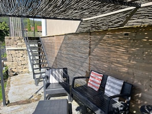 Ein Sitzbereich im Freien mit einer Holzbank und Stühlen, einer Steinmauer und einer Metalltreppe.