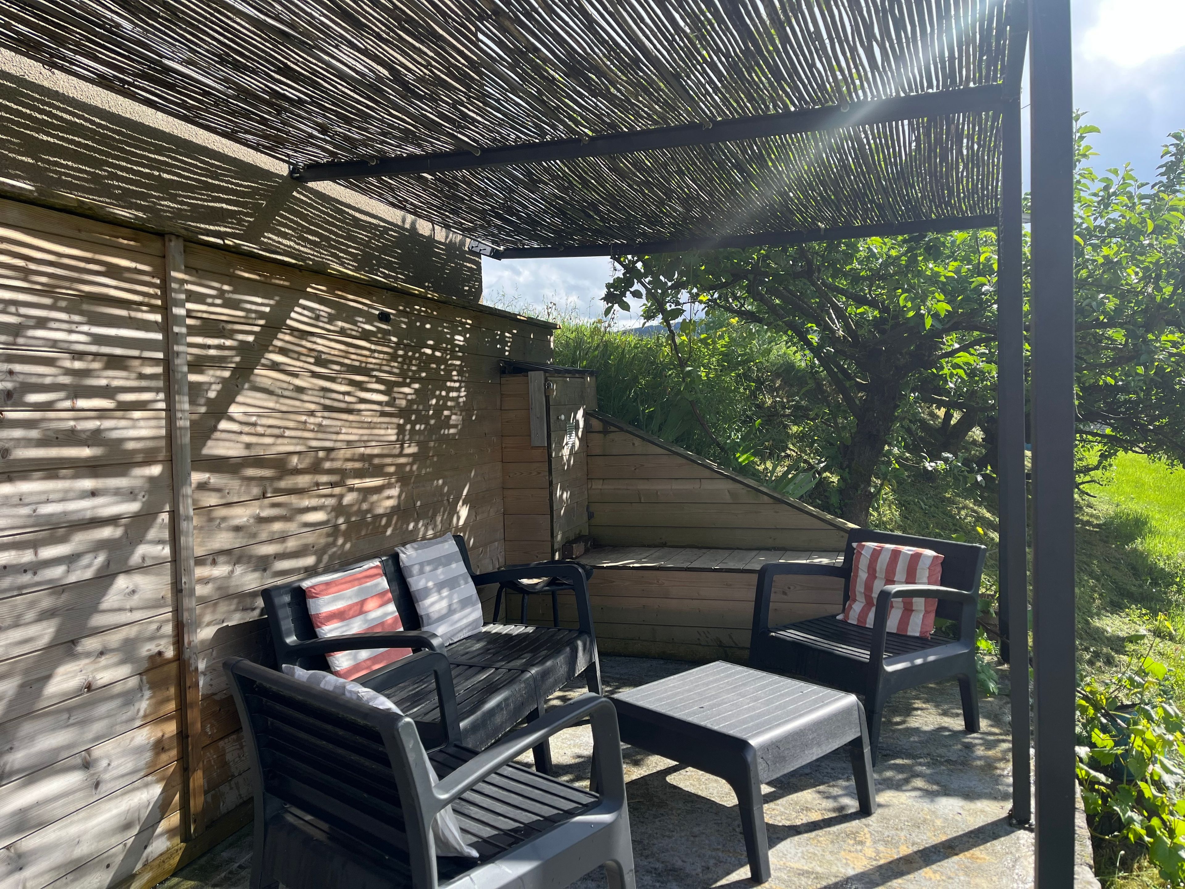 An outdoor seating area with two chairs and a table, a wooden wall, and a pergola structure.