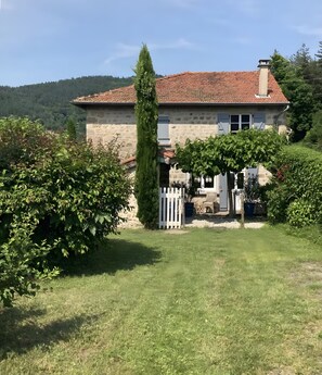 Una casa in pietra con tetto in tegole, circondata da un prato curato e diversi arbusti.