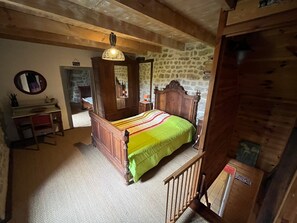 Una camera da letto con un letto di legno, uno specchio, una cassettiera e un muro in pietra.