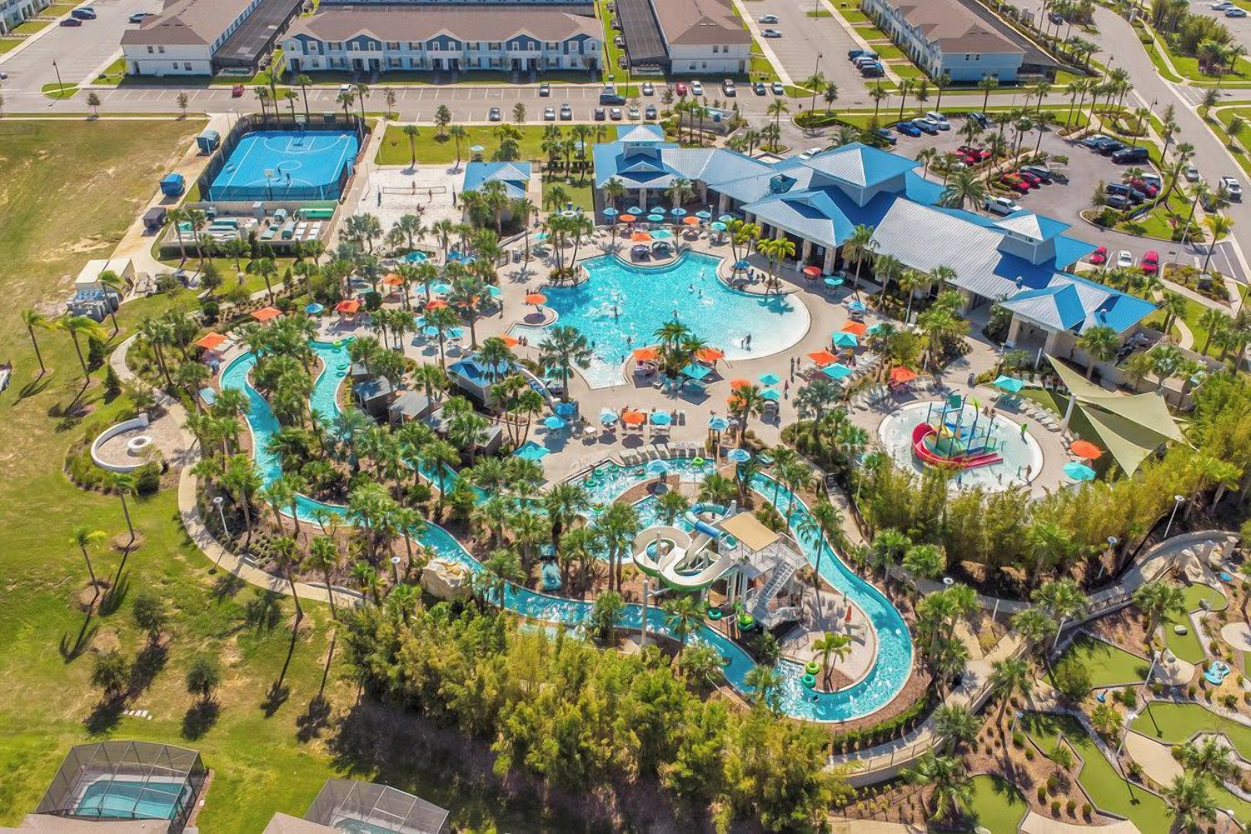 An aerial view of a resort with multiple swimming pools, palm trees, and a large building with a blue roof.