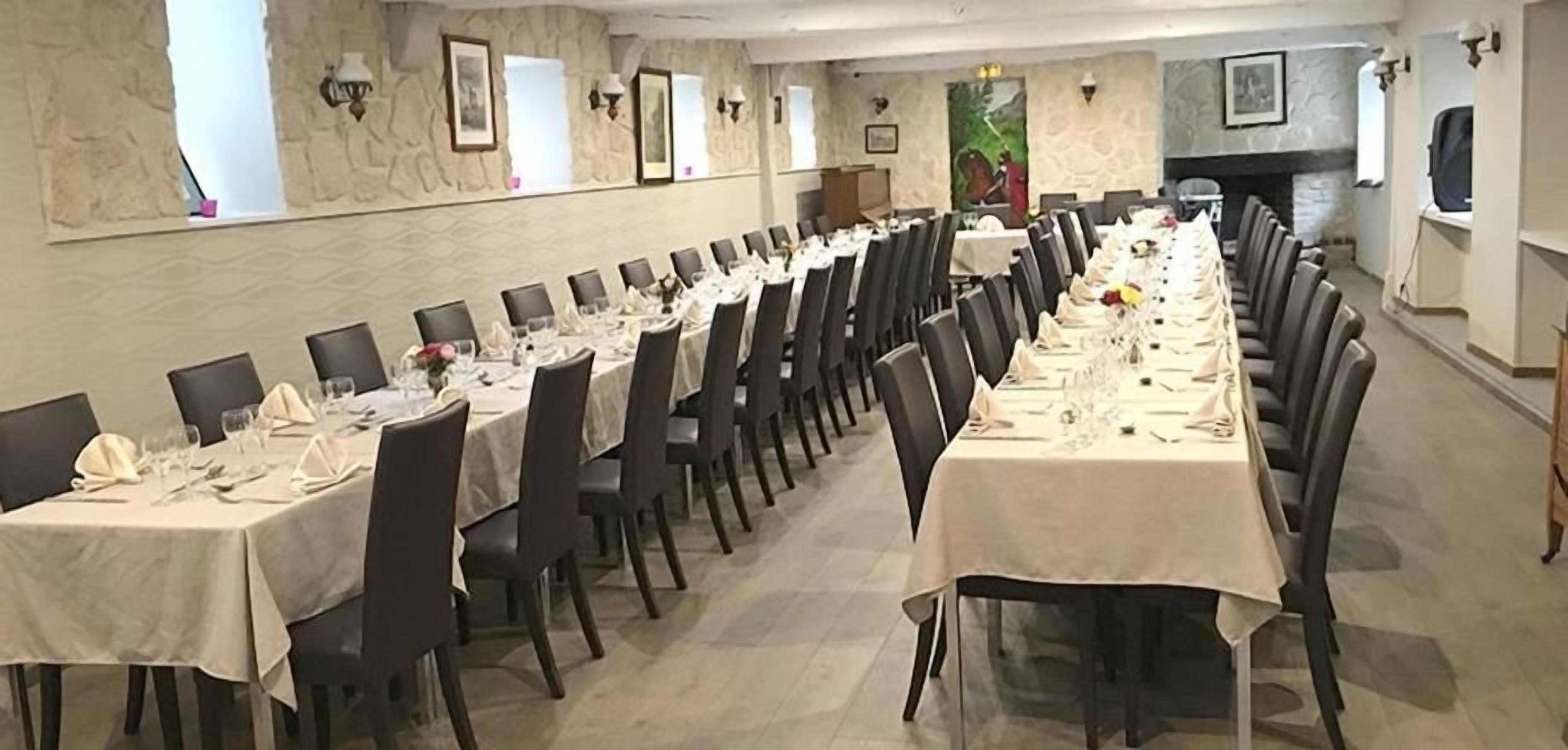 A long dining table with chairs, set for a meal, in a room with stone walls and framed pictures.