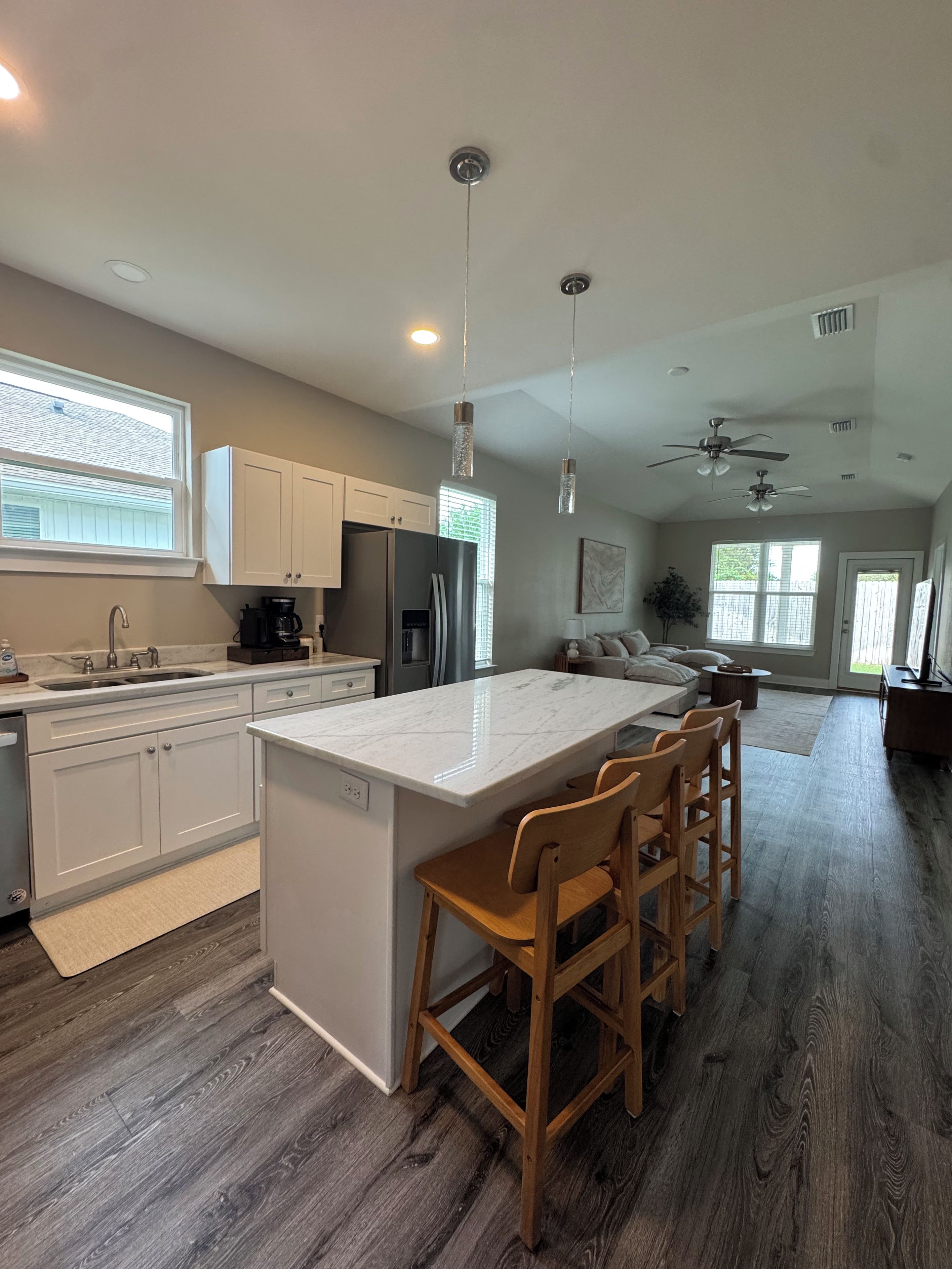 A modern kitchen with white cabinets, a central island with bar stools, a built-in refrigerator, and pendant lighting.