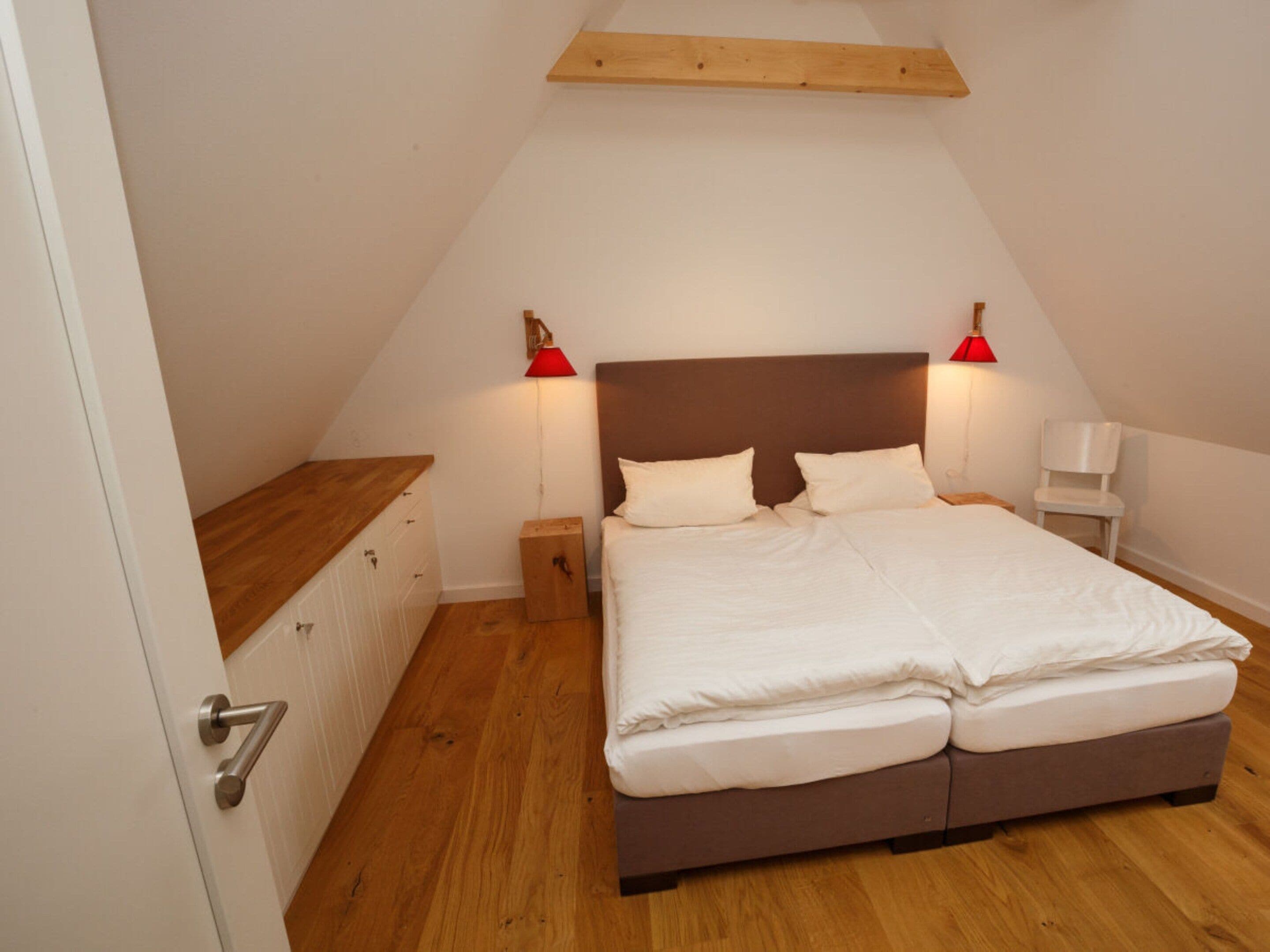 Ein Schlafzimmer mit einem Bett, Nachttischen, einem Sessel und einem Holzbalken an der Decke.