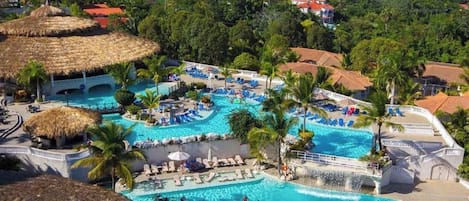 Un resort con varias piscinas, zonas de descanso y construcciones con techo de paja.
