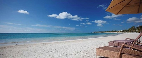 Una playa con arena blanca y agua cristalina. Se observan sillas de playa y una sombrilla.