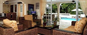 Un amplio espacio de sala con muebles de mimbre, una mesa de centro de vidrio y un televisor.