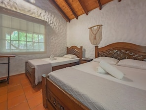 Un dormitorio con dos camas, una ventana y un tapiz de macramé en la pared.