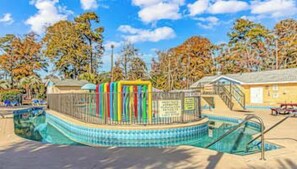 Una piscina amb una terrassa, envoltada d'arbres i un edifici.