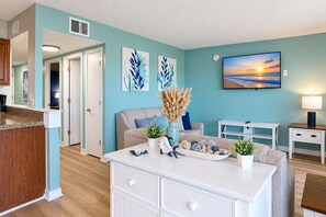 A modern living room with a kitchen island, a sofa, and a painting of a sunset. - Myrtle Beach Resort B-526 with Endless Myrtle Beach Adventures! (Myrtle Beach)