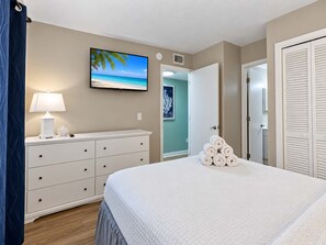 A bedroom with a bed, a nightstand with a lamp, a wall-mounted TV, and a door leading to another room. - Myrtle Beach Resort B-526 with Endless Myrtle Beach Adventures! (Myrtle Beach)