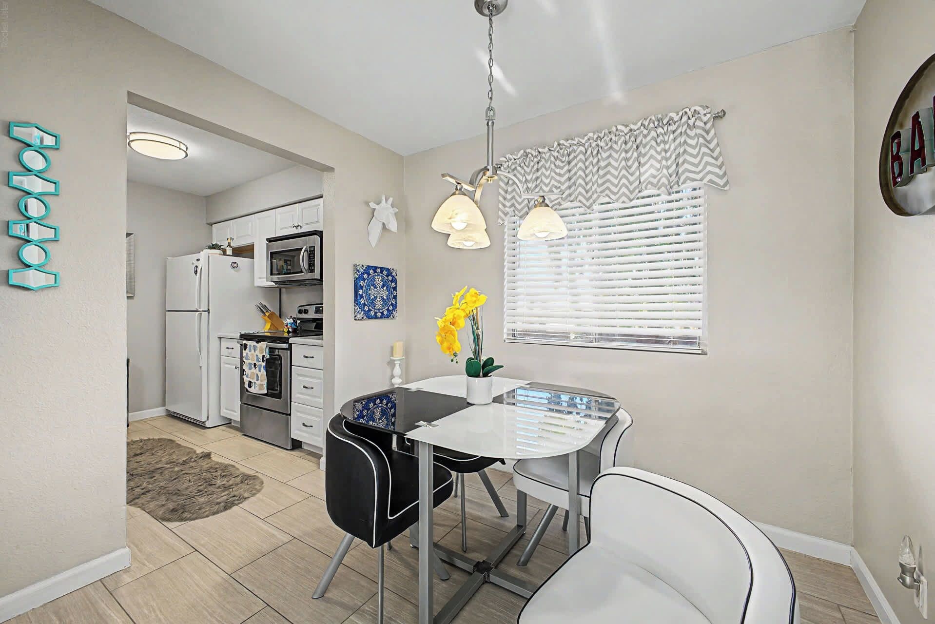 A modern kitchen with white cabinets, a refrigerator, an oven, and a dining area with a table and chairs.