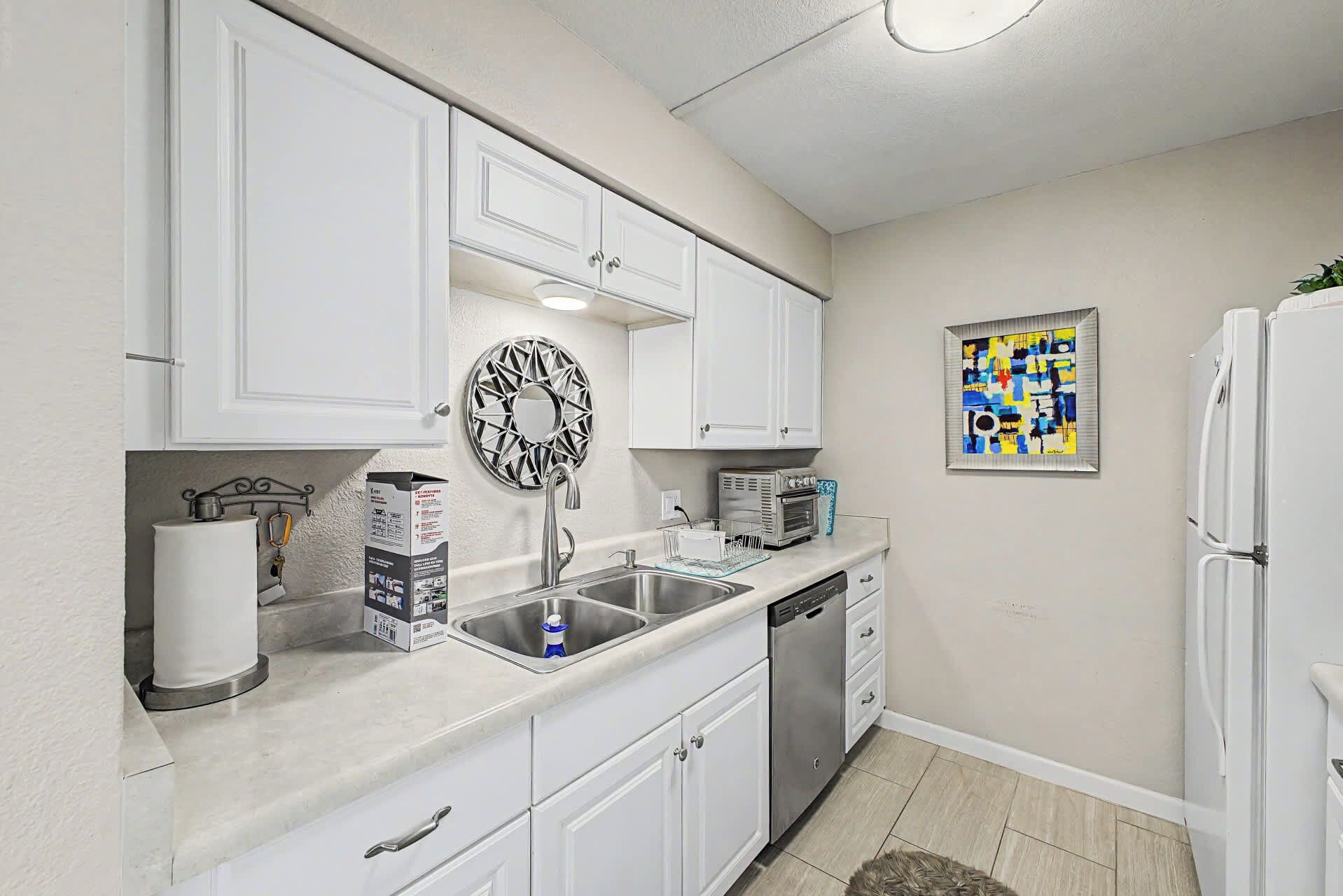 A compact kitchen with white cabinets, a stainless steel sink, a built-in oven, and a refrigerator.