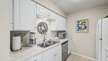 A compact kitchen with white cabinets, a stainless steel sink, a built-in oven, and a refrigerator.