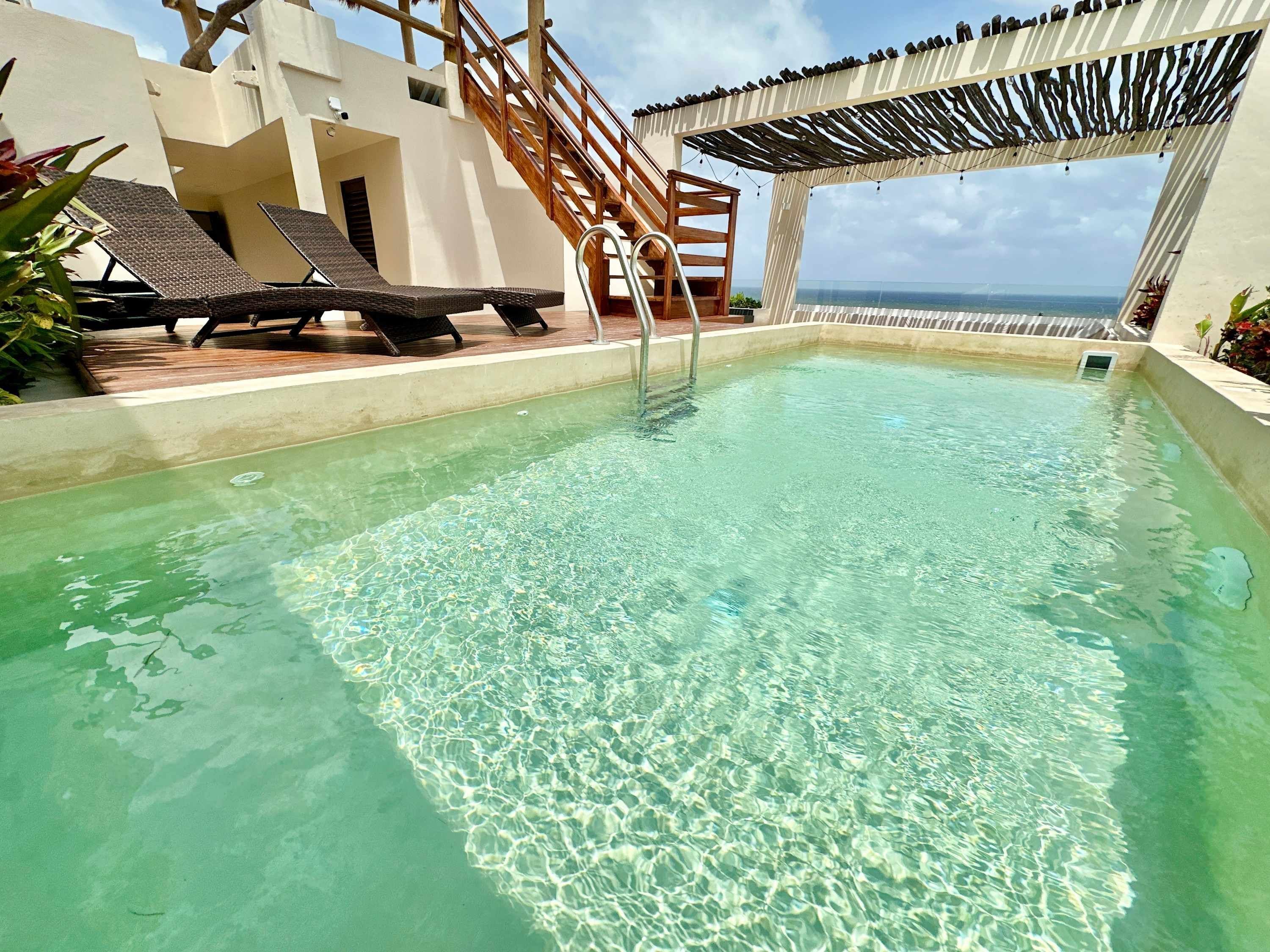 Ein klares Schwimmbecken mit einer Holzterrasse, Liegestühlen und einer Pergola mit Lichterketten.