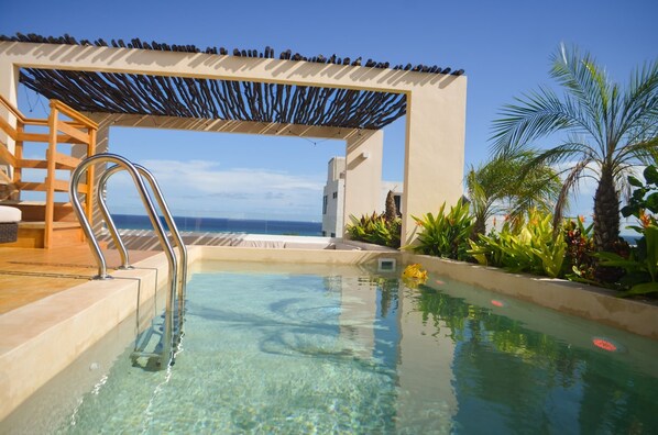 A clear pool with a metal ladder, a wooden pergola, and a view of the ocean. - Estudio arm  nico y esencia caribe  a  Cerca del mar (Playa del Carmen)