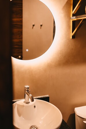 A bathroom with a round mirror, a sink, and a toilet. - Boutique studio just steps from the sea (Playa del Carmen)