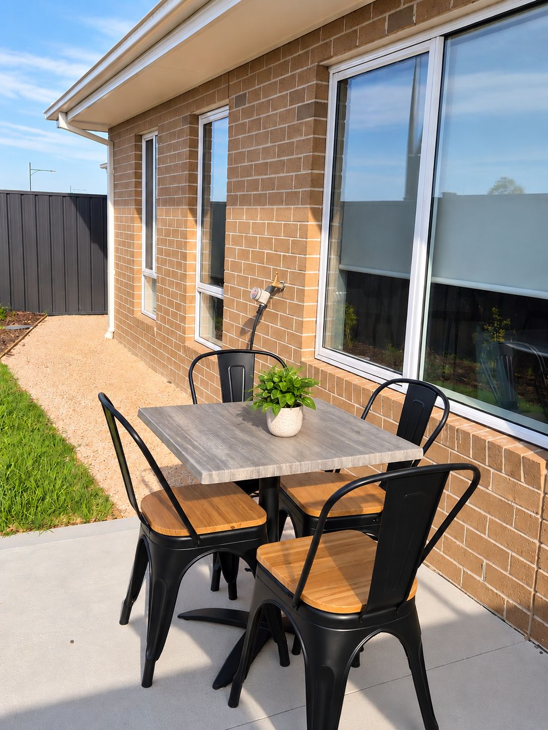 Une terrasse extérieure avec une table et des chaises, un pot de fleurs et un mur en briques.