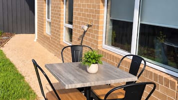 Une terrasse extérieure avec une table et des chaises, un pot de fleurs et un mur en briques.