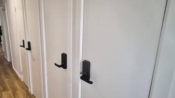 Una hilera de puertas blancas con manijas negras, suelo de madera y pared blanca.