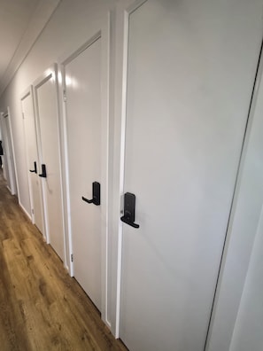 Una hilera de puertas blancas con manijas negras, suelo de madera y pared blanca.