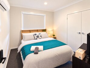A hotel room with a bed, a bedside table with a lamp, a TV, and a wardrobe. - Private Room & Own Bathroom (Cobblebank)
