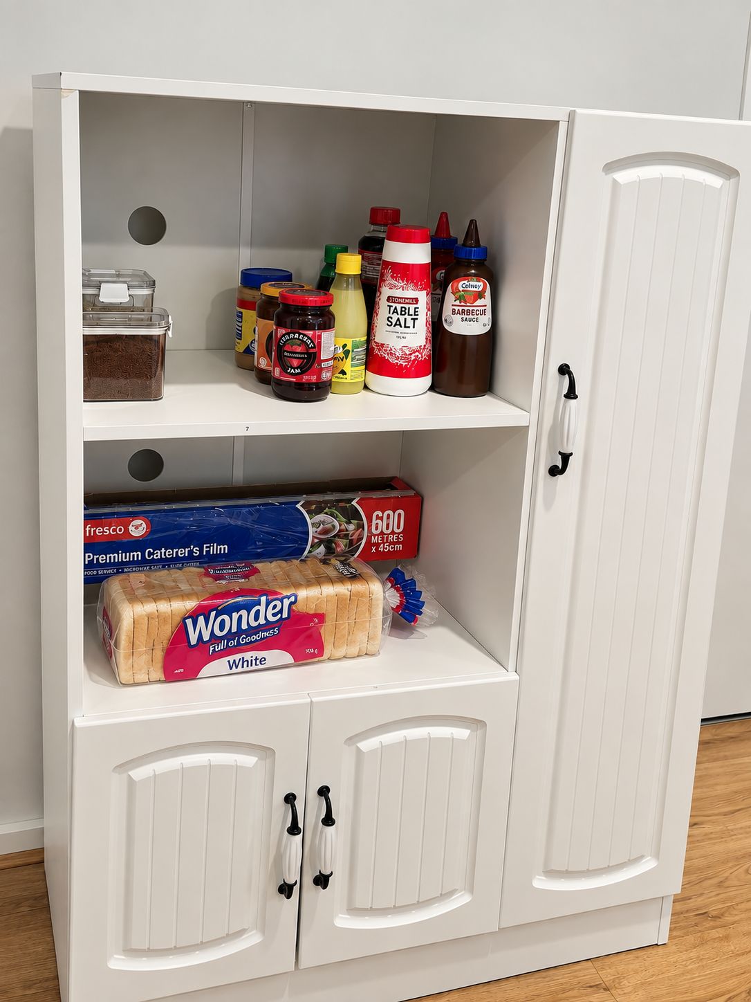 Un armario blanco con varios estantes que contiene diferentes alimentos y una caja de Wonder bread.