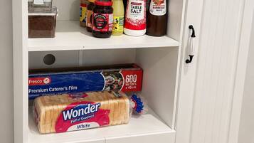 Un armario blanco con varios estantes que contiene diferentes alimentos y una caja de Wonder bread.