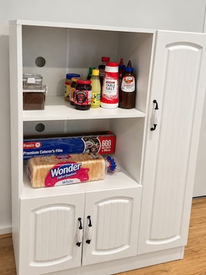 Un armario blanco con varios estantes que contiene diferentes alimentos y una caja de Wonder bread.