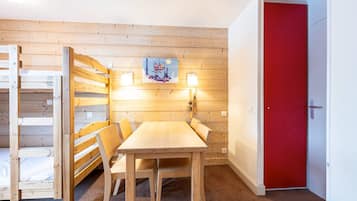Une pièce avec un lit superposé en bois, une table avec des chaises, une porte rouge et un luminaire fixé au mur.