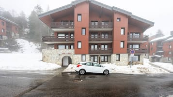 Un immeuble à plusieurs étages, doté d’une façade en pierre et de balcons en bois, avec une voiture garée devant et un panneau indiquant qu’il est interdit de se garer.
