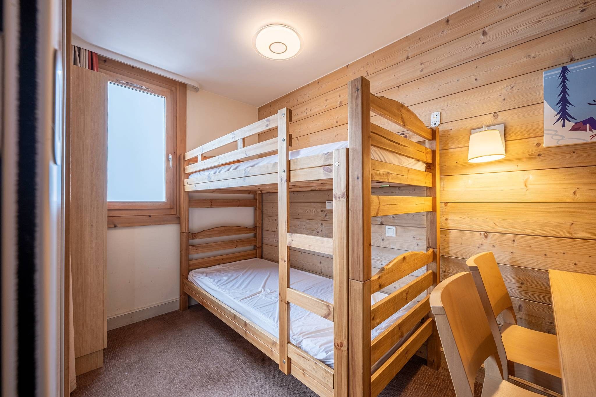 A bunk bed room with a window, a desk, and a chair.