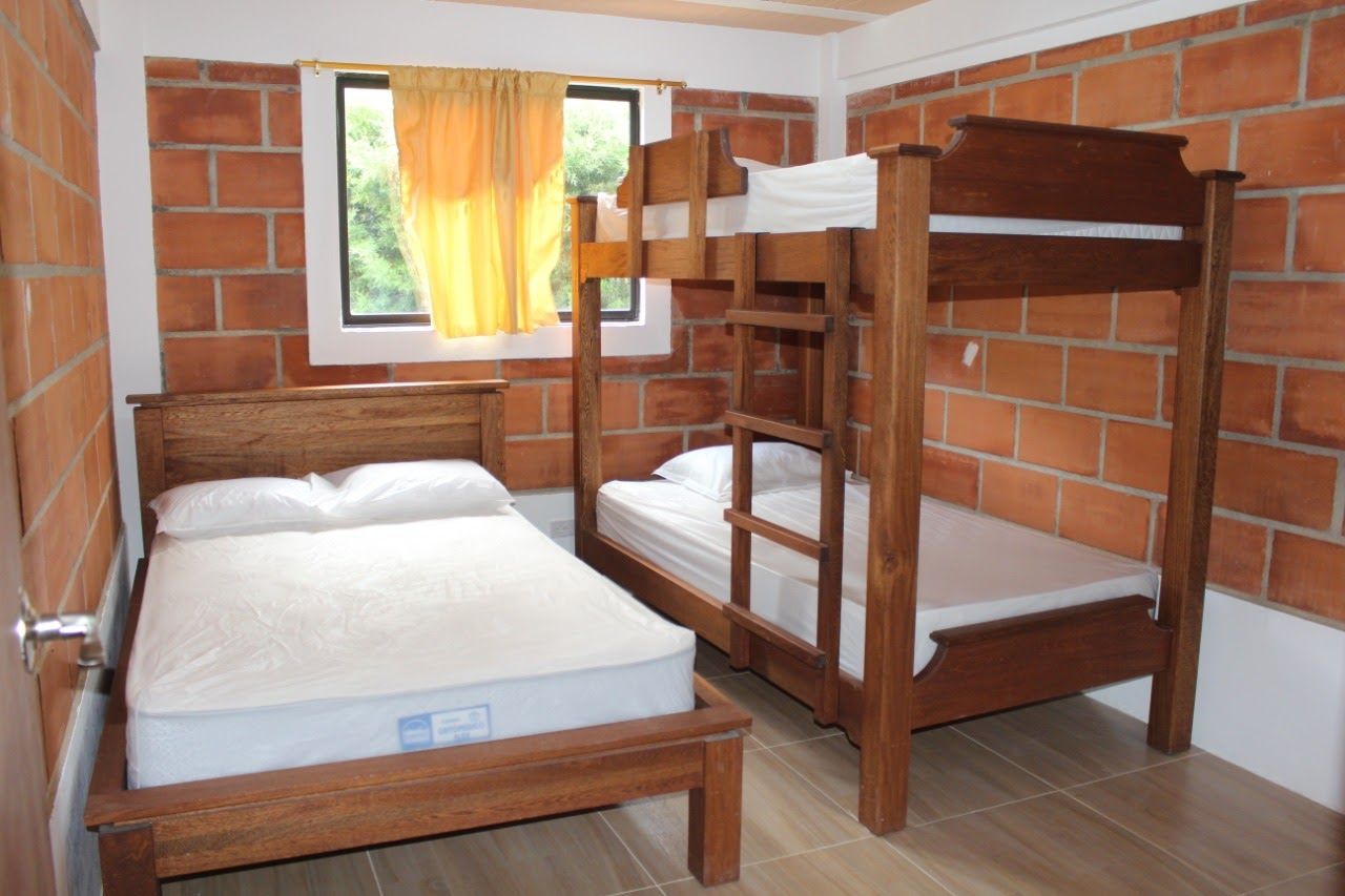 Ein Zimmer mit Backsteinwand, einem Vorhangfenster und einem Stockbett mit Matratze.