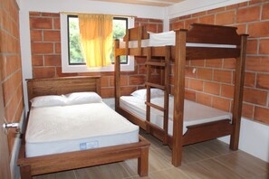 Een kamer met een bakstenen muur, een raam met gordijnen en een stapelbed met matras.