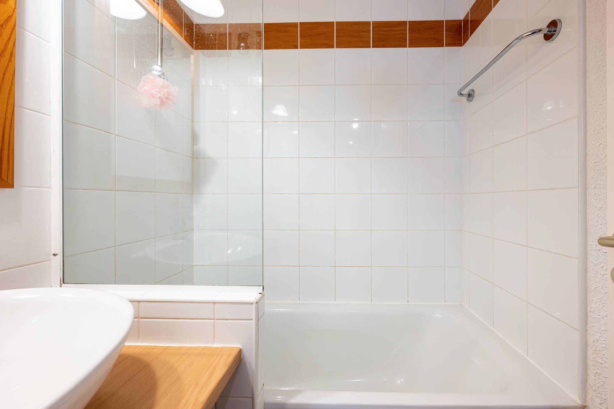A bathroom with a white sink, a wooden countertop, a white bathtub, and a shower area with a glass door.