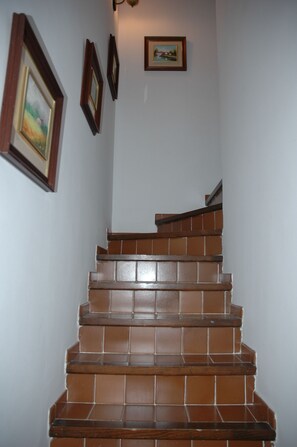 Un escalier recouvert de carreaux bruns menant à l’étage supérieur, flanqué de murs blancs et orné de tableaux encadrés.