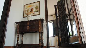 Un meuble en bois avec des tiroirs, un tableau accroché au-dessus, et une porte entrouverte donnant sur une pièce dont le mur est décoré de motifs.