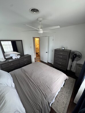 Une chambre à coucher avec un lit, une commode, un miroir, un ventilateur de plafond et un ventilateur.