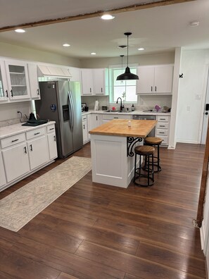 A modern kitchen with white cabinetry, a central island with stools, a stainless steel refrigerator, and a window with a view. - Spacious 3-bedroom house for Augusta Masters Week (Martinez)