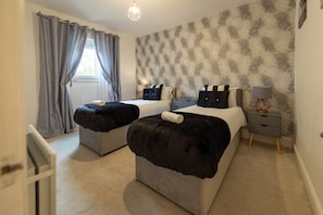 A double room with two beds, a window with curtains, a wall with a feather pattern, and a bedside table with a lamp. - Cosy Windsor Family Escape – Near LEGOLAND, Windsor Castle & London (Windsor)