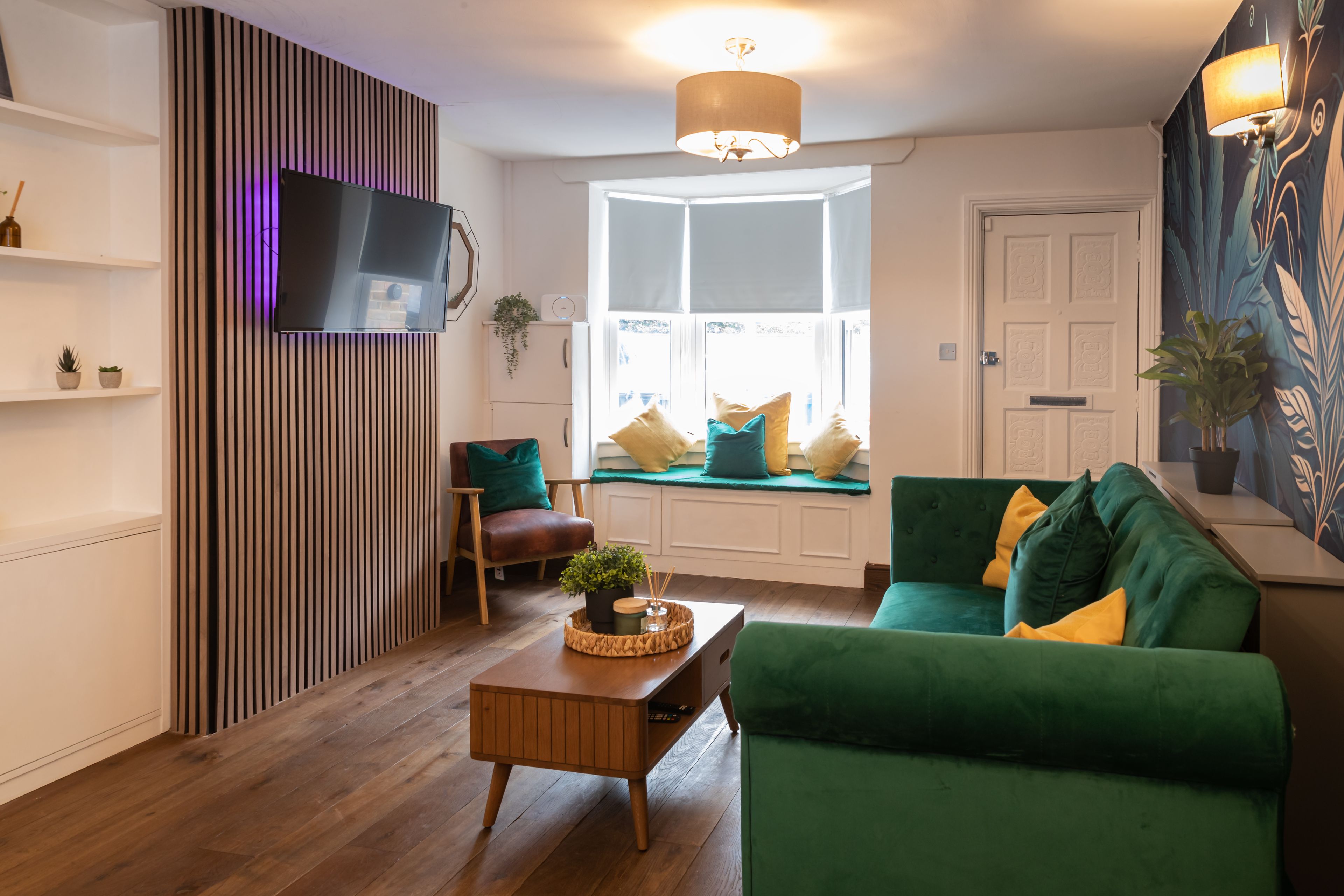 A modern living room with a green sofa, wooden coffee table, and a flat-screen TV mounted on a wall with vertical slats.